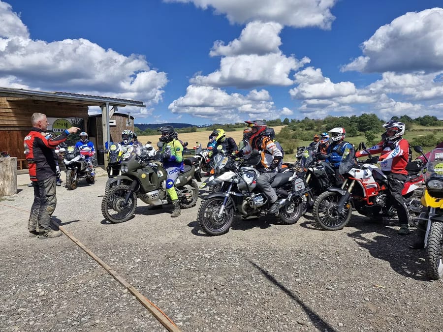 Fahrerbesprechung auf dem Gelände, Reiseenduros aufgereiht in der Sonne.