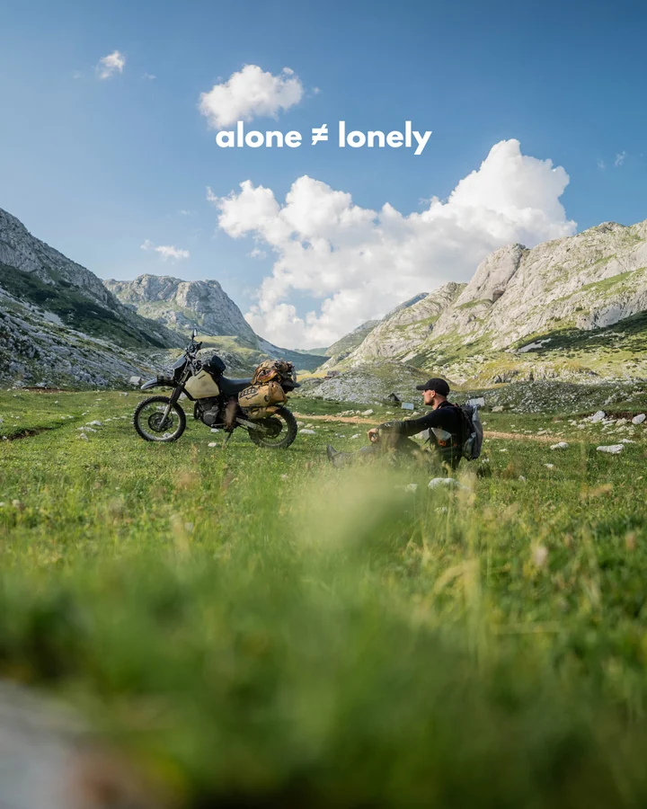 Alone: a rider with a loaded DR650 in an alpine meadow